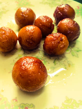 Gulab Jamun balls with sugar syrup placed in a white plate.They are made of bread while homemade.They are deep fried dumplings made of fried milk and dipped in rose cardamom flavored sugar syrup.の写真素材