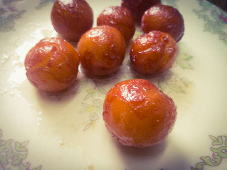 Gulab Jamun balls with sugar syrup placed in a white plate.They are made of bread while homemade.They are deep fried dumplings made of dried milk and dipped in rose cardamom flavored sugar syrup.の写真素材