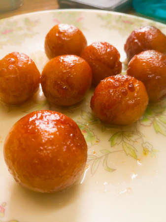 Gulab Jamun balls with sugar syrup placed in a white plate.They are made of bread while homemade.they are deep fried dumplings made of fried milk and dipped in rose cardamom flavored sugar syrup.の写真素材