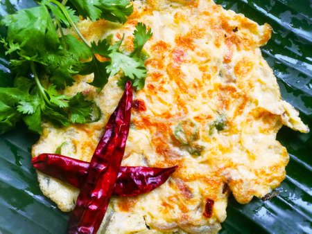 Omelette with coriander leaves and Red chillies in a banana leaf.The banana leaf has green color and the chillies are red in color and the omelette is fried well.The banana leaf has lines on itの写真素材