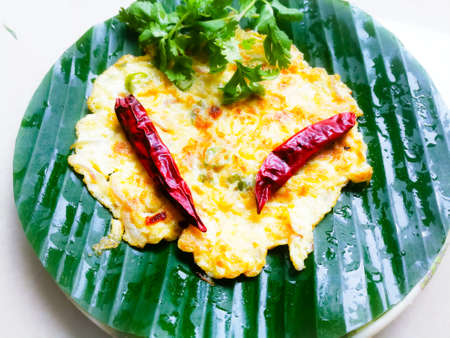 Omelette with coriander leaves and Red chillies in a banana leaf.The banana leaf has green color and the chillies are red in color and the omelette is fried well.The banana leaf has lines on itの写真素材
