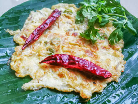 Omelette with coriander leaves and Red chillies in a banana leaf.The banana leaf has green color and the chillies are red in color and the omelette is fried well.The banana leaf has lines on itの写真素材