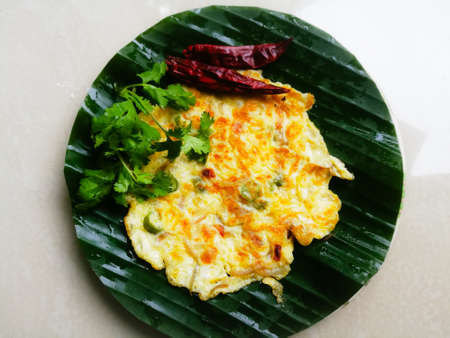 Omelette with coriander leaves and Red chillies in a banana leaf.The banana leaf has green color and the chillies are red in color and the omelette is fried well.The banana leaf has lines on itの写真素材