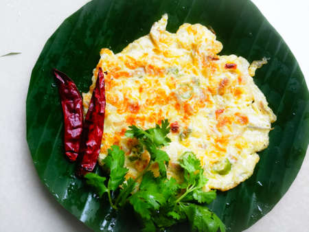 Omelette with coriander leaves and Red chillies in a banana leaf.The banana leaf has green color and the chillies are red in color and the omelette is fried well.The banana leaf has lines on itの写真素材
