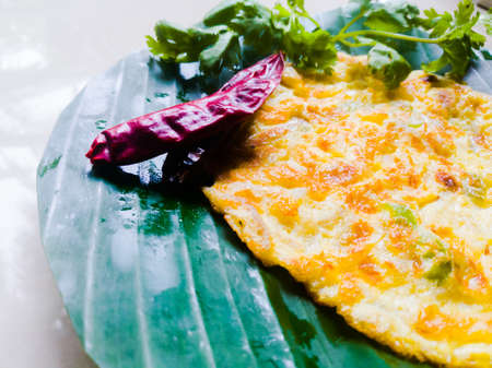 Omelette with coriander leaves and Red chillies in a banana leaf.The banana leaf has green color and the chillies are red in color and the omelette is fried well.The banana leaf has lines on itの写真素材