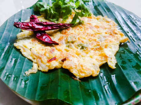 Omelette with coriander leaves and Red chillies in a banana leaf.The banana leaf has green color and the chillies are red in color and the omelette is fried well.The banana leaf has lines on itの写真素材