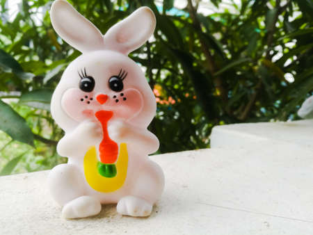 Toy Rabbit of small size in white color and have black eyes.The rabbit has two large ears and a carrot is hanging in its mouth.It also has red cheeks and it is in sitting position.の写真素材