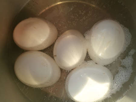 Boiling eggs in a steel vessel and the bubbles are coming up.The eggs are partially under the water and the bubbles are formed near to the eggs.There are five eggs in it.の写真素材