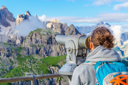 Young woman looking through binoculars at the wonderful view of the Dolomites Mountains, Dolomiti di Sesto or Sextner Dolomites, Italyの写真素材