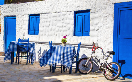 KALMNOS, GREECE- MAY 1, 2015: Typical Greek restaurant with blue tables and chairs and small bike parkedのeditorial素材