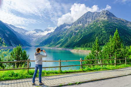 Young woman photographing a beautiful alpine lake, Zillertal, Austriaの写真素材