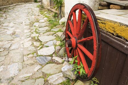Old wooden red wagon wheel on stone footpathの写真素材