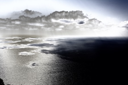 Dark clouds with sun rays reflecting over sea waterの写真素材
