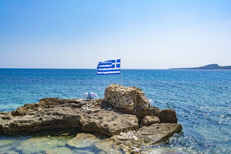 Traditional chairs with a table of a traditional tavern at the beautiful Greek village of Marathopolis located in Messinia - Greece. Near the table is a Greek flag.の写真素材