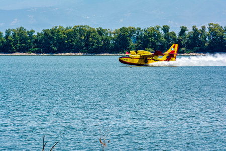 A yellow firefighting plane skims the surface of Lake Kerkini in Greece, collecting water for firefighting operations.の写真素材