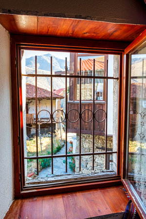 A view through a traditional wooden-framed window in Elati, Trikala, Greece, showcasing the village's stone houses and tiled rooftops with mountainous scenery.の写真素材