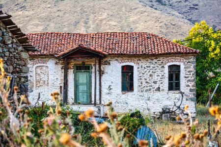 A charming old stone cottage with a red-tiled roof and green door in Agios Germanos, Greece, reflecting traditional rural architecture against a mountainous landscape.の写真素材