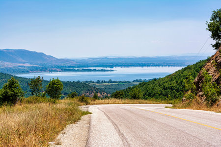 A winding road descends through hills towards Lake Kastoria, offering panoramic views of the lake and surrounding landscape in Greece.の写真素材