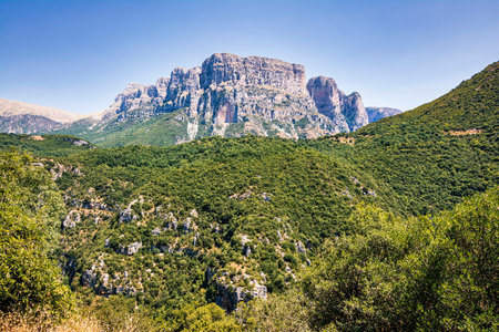 Panoramic view of the Vikos Gorge and surrounding mountains in Zagori, Greece, showcasing lush green...