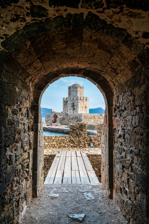 The iconic Bourtzi Tower at Methoni Fortress, viewed through a stone archway with a wooden bridge leading toward the historic structure.の写真素材