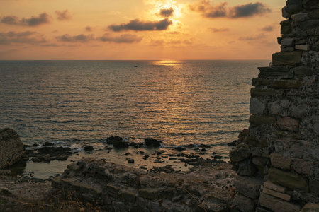A serene rocky shoreline below Methoni Fortress bathed in warm sunlight reflecting on the Ionian Sea during a picturesque sunset.の写真素材