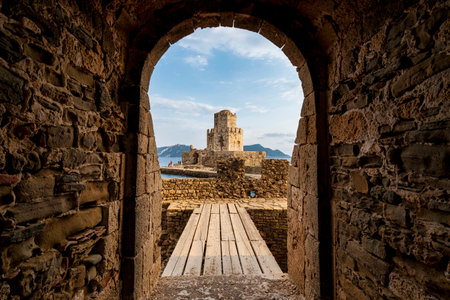 The iconic Bourtzi Tower at Methoni Fortress, viewed through a stone archway with a wooden bridge...
