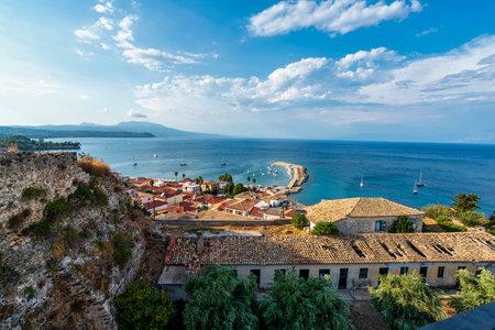 A breathtaking panoramic view of Koroni harbor with tiled rooftops, a winding pier, anchored boats, and the serene Mediterranean Sea.の写真素材