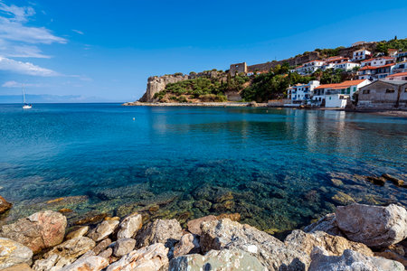 Scenic seaside view of Koroni, featuring turquoise waters, historic ruins, rocky shoreline, and...