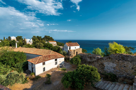 A serene view of the Iera Moni Timiou Prodromou monastery complex in Koroni, featuring tiled rooftops, lush greenery, and the Mediterranean Sea.の写真素材