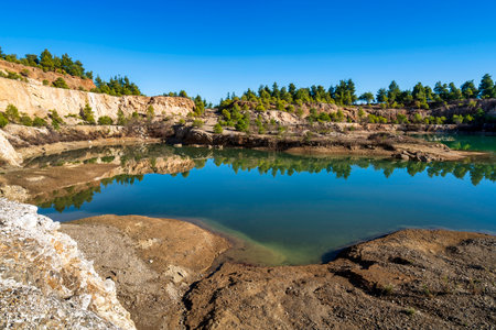 A scenic artificial lake formed in an abandoned mining quarry in Evia, Greece, reflecting rocky...