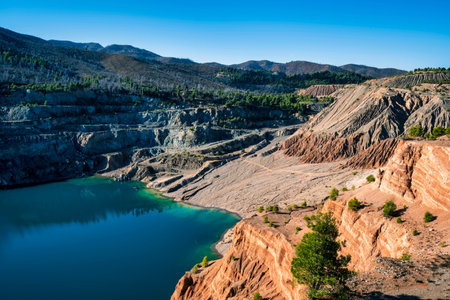 A deep blue artificial lake in an abandoned quarry in Evia, Greece, surrounded by layered rock formations, rugged terrain, and forested hills.の写真素材