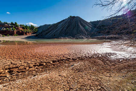 A partially dried artificial lake in an abandoned quarry in Evia, Greece, featuring cracked earth,...
