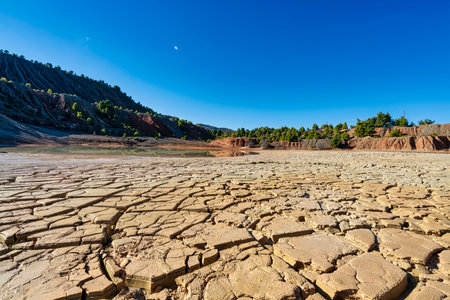 A partially dried artificial lake in an abandoned quarry in Evia, Greece, featuring cracked earth,...