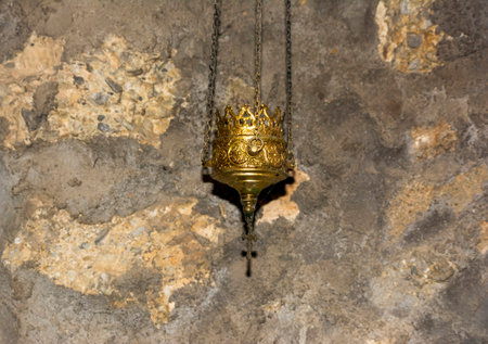 Close-up of a detailed golden incense lamp hanging against the rough stone wall of an ancient...