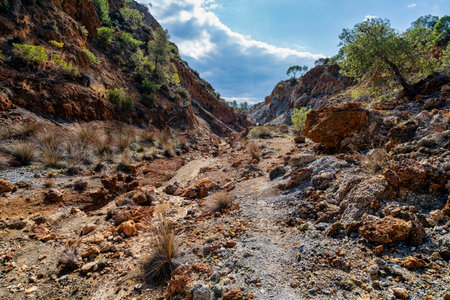 Rugged volcanic valley filled with scattered rocks, sparse vegetation, and steep cliffs at Sousaki Volcano near Corinth, Greece.の写真素材