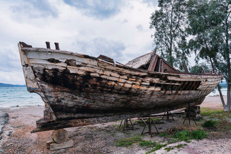 A weathered and decaying wooden fishing boat rests on supports by the sea in the harbor of Nea...