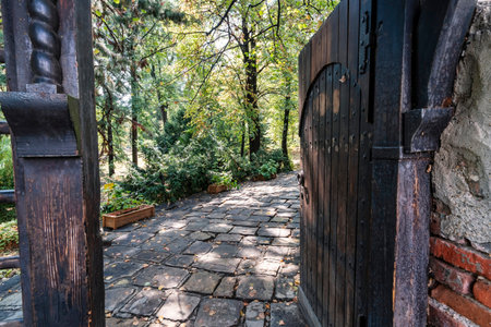 Open wooden gate leads to cobblestone path and lush garden surrounding Boyana Church in Sofia,...