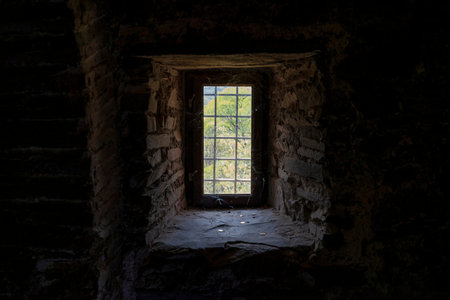 A narrow stone window with iron bars and coin offerings sits in darkness inside Asen Fortress near Asenovgrad, Bulgaria.の写真素材