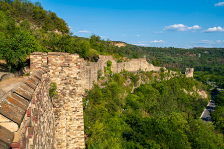 Panoramic view of the long medieval stone walls of Tsarevets Fortress stretching along a forested...