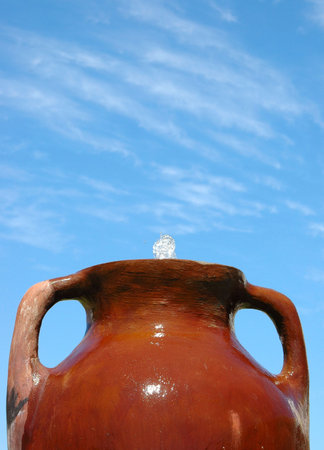A big brown terracotta pot with a little waterfall fountain in front of blue sky backgroundの写真素材