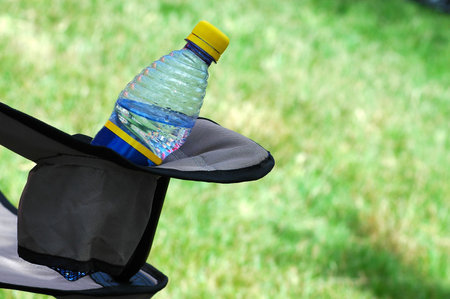A bottle of sparkling mineral water in a camping chair for picnic refreshment outdoors in summerの写真素材