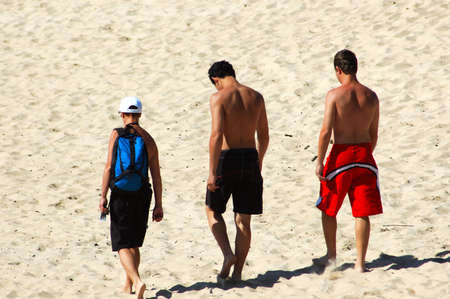 Three young men walking in the sand on the beachの写真素材