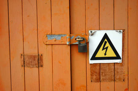 A brown wooden locked door with a danger sign (black and yellow triangle with flash) keeping a secret locked behind doorsの写真素材