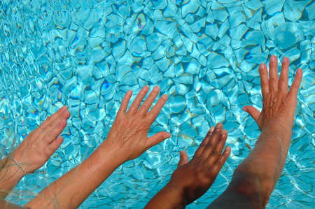 African black and caucasian white hands reaching the water while women jumping into the swimming-pool in summerの写真素材