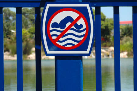A blue metal fence with a no swimming sign in front of a lakeの写真素材