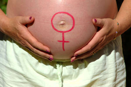 Two white hands of a caucasian pregnant woman holding her big belly with a red girl symbol on outdoors in summerの写真素材