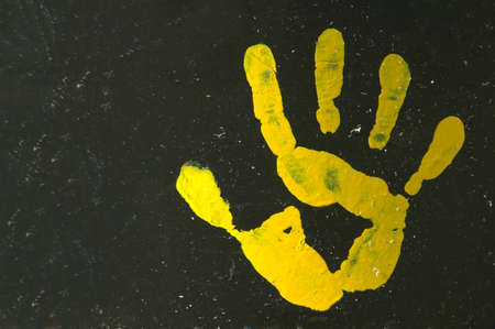 A yellow painted open hand print with five fingers on a black background of an old garbage drum の写真素材