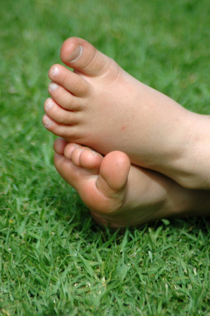 Two little white healthy feet of a caucasian child resting barefeet in the grass of a tidy lawn in the sunshine outdoors during summertime の写真素材