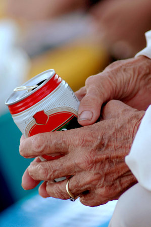 Two wrinkled aged hands of an elderly caucasian white woman holding a can of beer outdoors の写真素材
