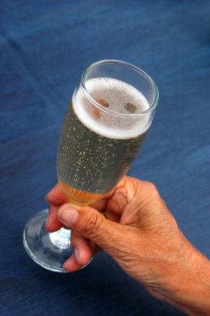 An elderly female hand of an old woman with a full champagne glass on blue tablecloth の写真素材